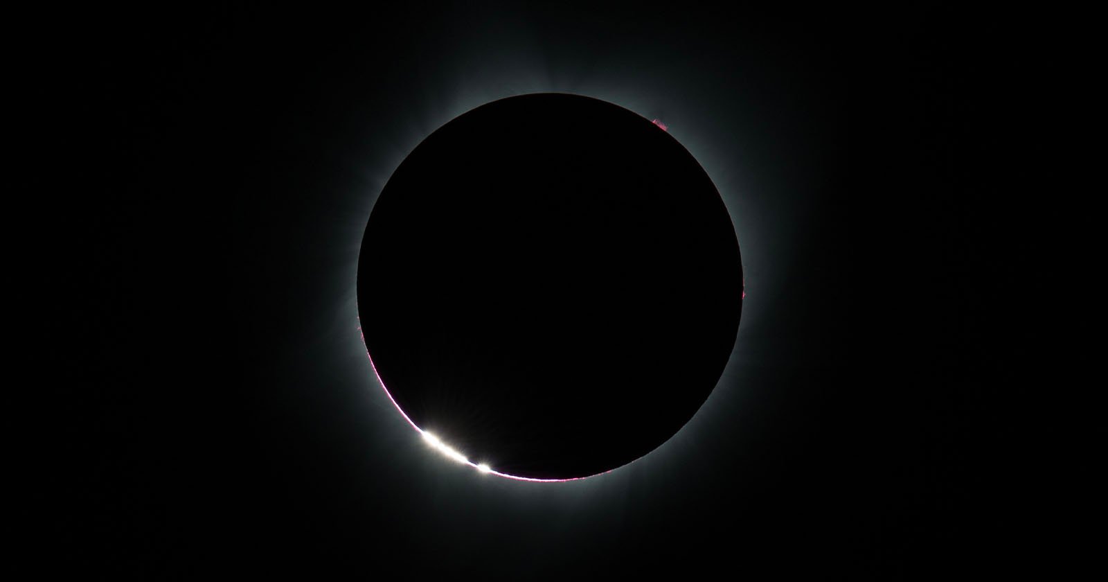 An solar eclipse with the Baily's beads phenomenon, where light rays peak out at the edge, is shown.